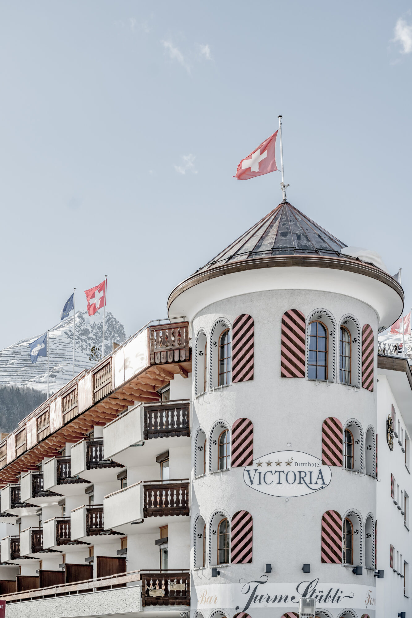 Verschneiter Turm des Turmhotel Victoria in Davos vor einer winterlichen Bergkulisse