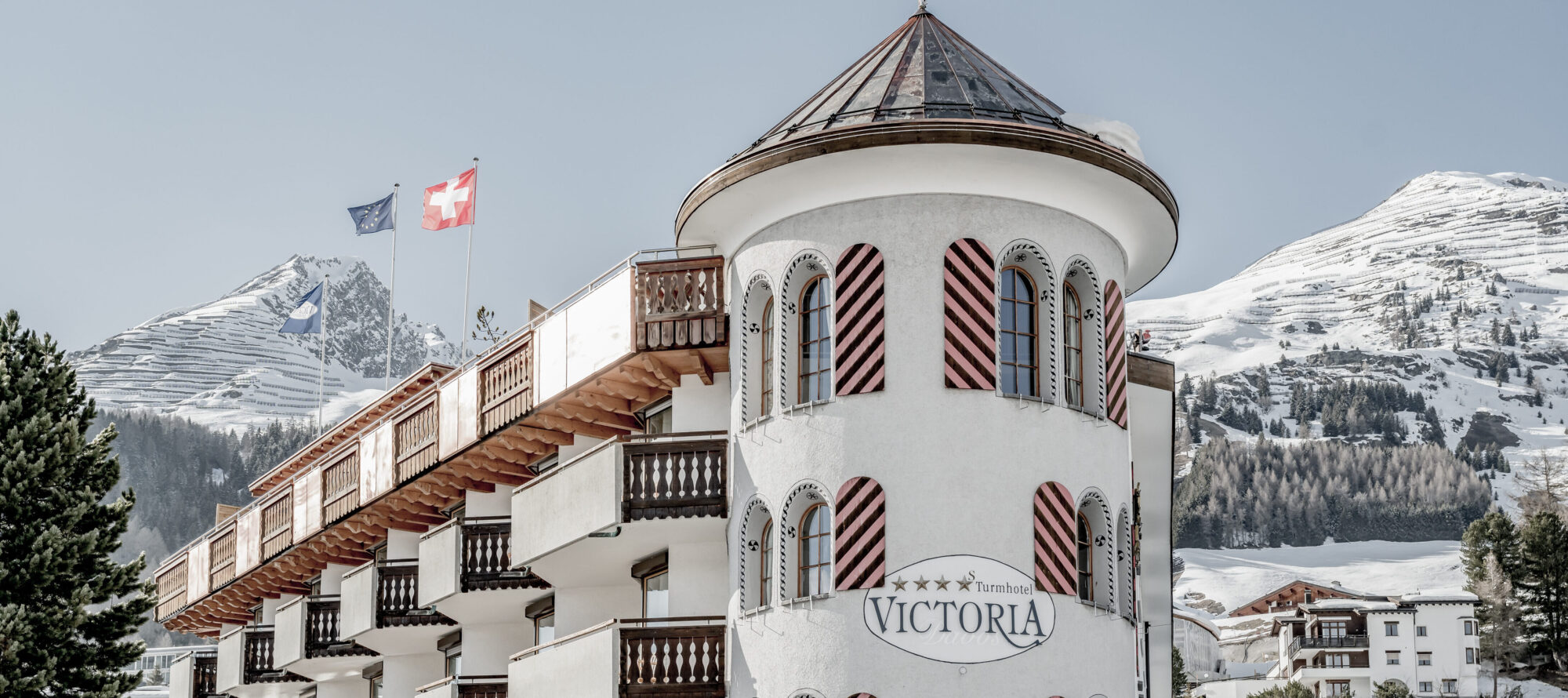 Verschneiter Turm des Turmhotel Victoria in Davos vor einer winterlichen Bergkulisse